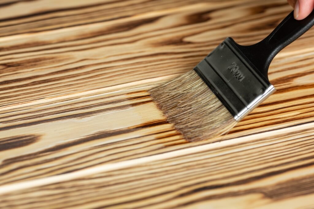 A Stain Is Applied To The Burnt Wooden Base With A Brush