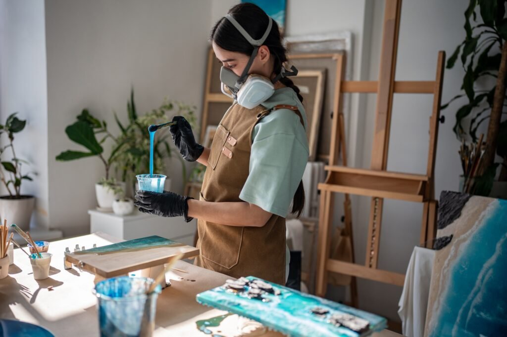 Artisan in respirator stirs epoxy resin with pigment, creating consistency for painting in workshop