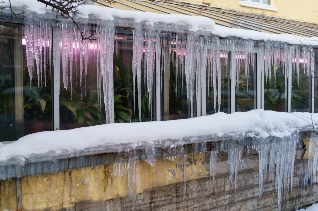 Old greenhouse building with icicles hanging down from roof during freeze and thaw cycles in winter